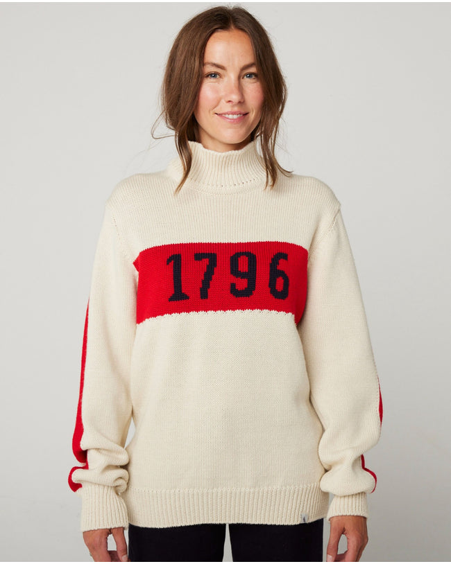 Flatlay image of Ecru knitted wool jumper with red stripe across the chest, detailing the numbers 1796 in black.