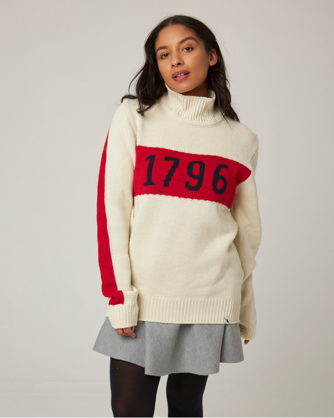 Flatlay image of Ecru knitted wool jumper with red stripe across the chest, detailing the numbers 1796 in black.