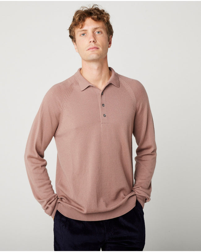 A flatlay image of a beige/ oatmeal polo shirt jumper. The jumper has a collar and  4 buttons to the chest. The hem and cuff have a ribbed detail. The jumper is a light weight, fine knit jumper and only one colour all over. A male model wearing the beige jumper with beige trousers and black shoes. He is smiling at the camera and has one hand in his trouser pocket.