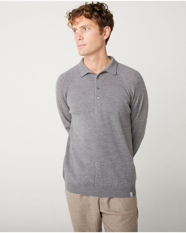 A flatlay image of a grey polo shirt jumper. The jumper has a collar and  4 buttons to the chest. The hem and cuff have a ribbed detail. The jumper is a light weight, fine knit jumper and only one colour all over. A male model wearing the jumper with all of the button done up and looking to the right.