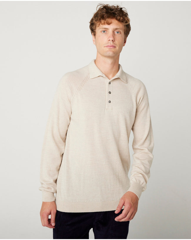 A flatlay image of a beige/ oatmeal polo shirt jumper. The jumper has a collar and  4 buttons to the chest. The hem and cuff have a ribbed detail. The jumper is a light weight, fine knit jumper and only one colour all over. A male model wearing the beige jumper with beige trousers and black shoes. He is smiling at the camera and has one hand in his trouser pocket.