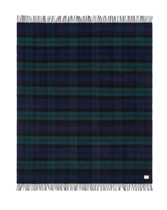 Flatlay image of a wool blanket folded into a small rectangle, the edge of the blanket is fringed, the blanket is multi-coloured check with alternating shades of navy and forest green. Image of the blanket laid out flat with fringing on both edges.