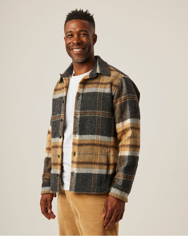 Flatlay image of a checked wool collared shirt with eight black buttons fastening down the front center of the shirt, it is a checked pattern consisting of a dark grey and sand as the main base colours and a white thin strip running through the squares.