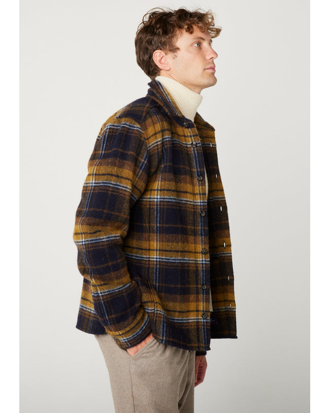 Flatlay image of a checked wool collared shirt with seven black buttons fastening down the front center of the shirt, it is a checked pattern consisting of navy, mustard and white rim around the squares.