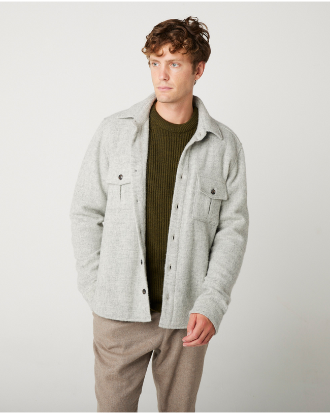 Flatlay image of a light grey wool collared shirt with seven small black buttons fastening down the center front fastening the shirt closed, the shirt has two discreet pockets on the either front bottom side of the shirt.