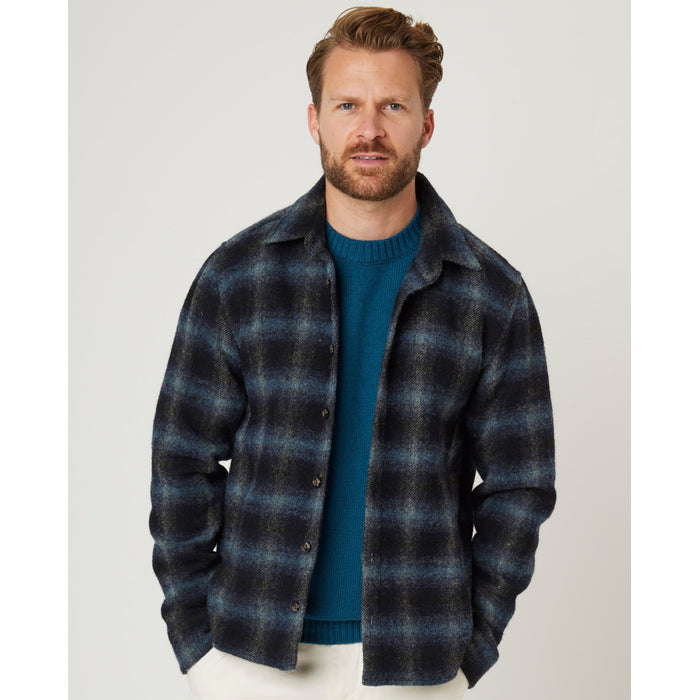 Flatlay image of a navy checked wool shirt with seven buttons down the center front fastening the collared shirt closed, the shirt has a slightly curved hem, the main base colour of the shirt is navy with the check pattern being a lighter shade of grey/blue.