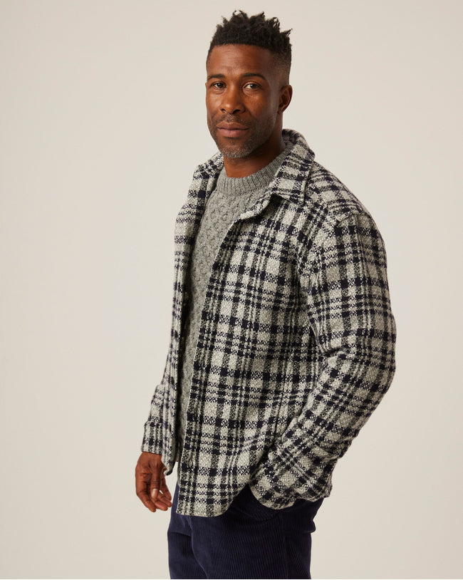 Flatlay image of light grey and black checked wool shirt with seven buttons down the center front fastening the collared shirt closed, the shirt has a slightly curved hem.